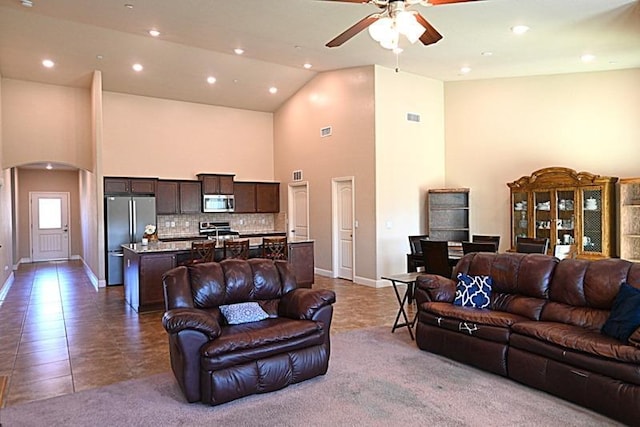 carpeted living room featuring visible vents, arched walkways, high vaulted ceiling, and a ceiling fan