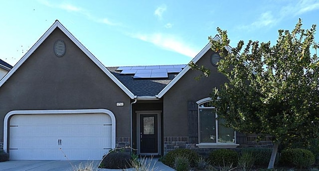 view of front facade with roof with shingles, driveway, stucco siding, a garage, and roof mounted solar panels