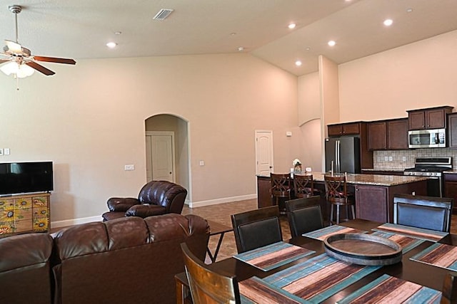 interior space featuring visible vents, high vaulted ceiling, a ceiling fan, arched walkways, and baseboards