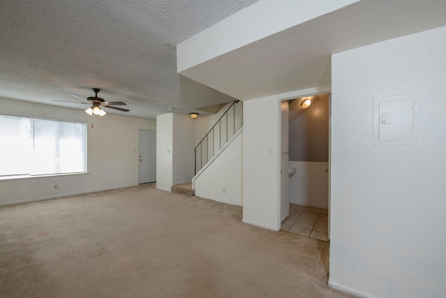 unfurnished living room with light carpet, stairway, a textured ceiling, and a ceiling fan