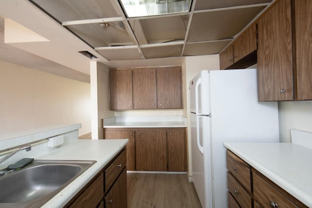 kitchen with light wood-type flooring, light countertops, brown cabinets, freestanding refrigerator, and a sink