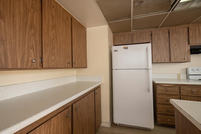 kitchen featuring white appliances, brown cabinetry, exhaust hood, and light countertops