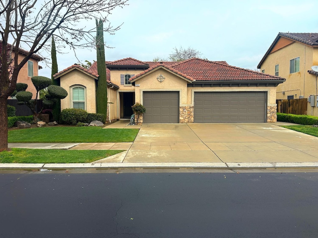 mediterranean / spanish house with driveway, an attached garage, stucco siding, stone siding, and a tile roof