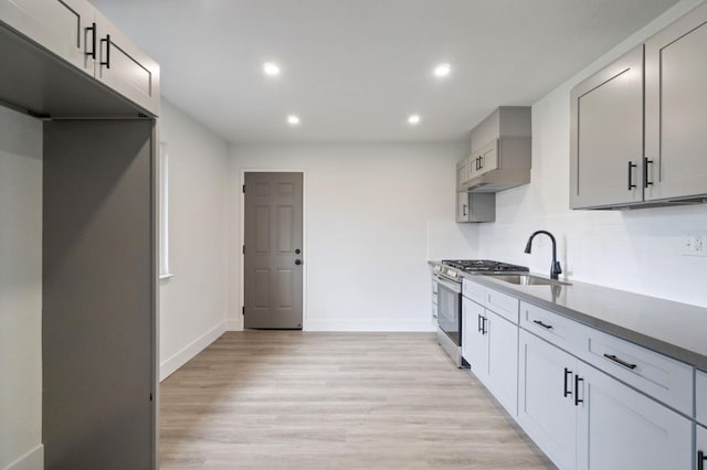 kitchen with a sink, gas range, backsplash, and light wood finished floors