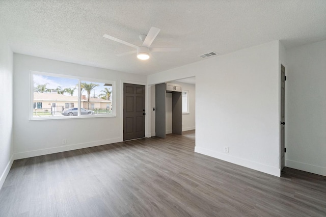 empty room with dark wood finished floors, a ceiling fan, visible vents, and baseboards