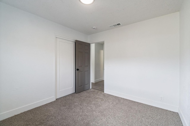 carpeted empty room featuring visible vents, baseboards, and a textured ceiling