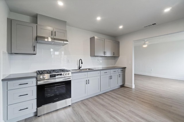 kitchen with stainless steel gas stove, gray cabinetry, light wood-style flooring, under cabinet range hood, and a sink