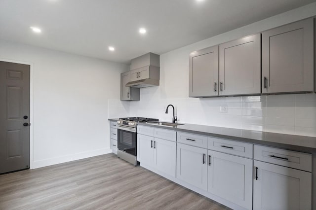 kitchen with gray cabinetry, light wood-style flooring, a sink, backsplash, and stainless steel range with gas cooktop