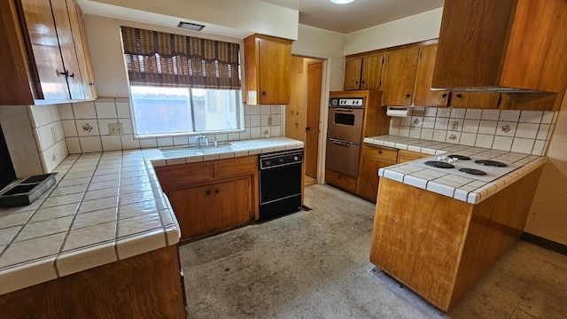 kitchen with range hood, brown cabinetry, a sink, tile counters, and dishwasher