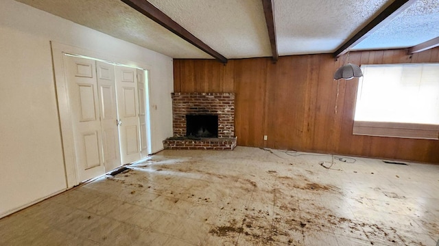 unfurnished living room featuring beamed ceiling, wood walls, a fireplace, and a textured ceiling