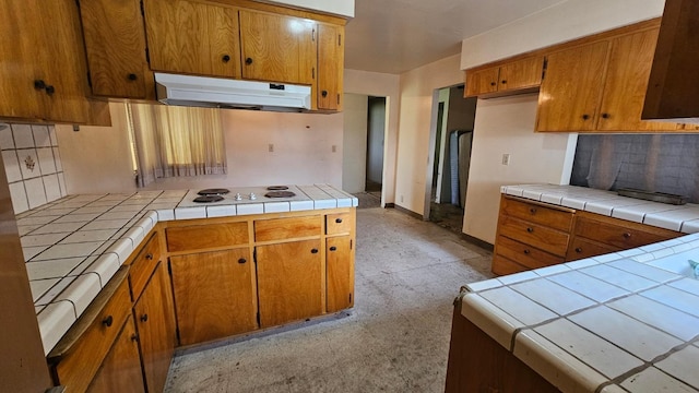 kitchen with brown cabinets, under cabinet range hood, white electric cooktop, decorative backsplash, and tile counters