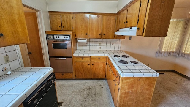 kitchen with under cabinet range hood, white electric stovetop, brown cabinetry, and tile countertops