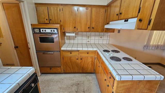 kitchen featuring under cabinet range hood, tile countertops, double oven, and light floors