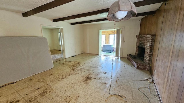 unfurnished living room featuring a brick fireplace, beamed ceiling, light floors, and a textured ceiling