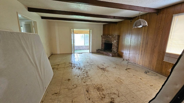 unfurnished living room featuring beam ceiling, a textured ceiling, wooden walls, a fireplace, and light floors