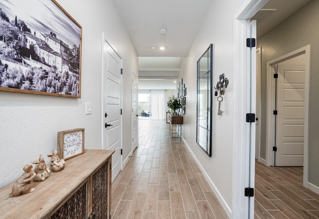 hall with a textured wall, baseboards, and wood tiled floor