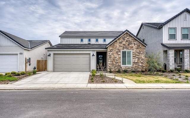 view of front of home featuring driveway, stone siding, fence, roof with shingles, and a garage