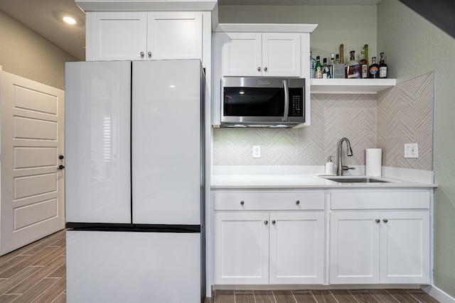 kitchen with a sink, stainless steel microwave, white cabinetry, freestanding refrigerator, and wood tiled floor