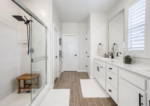 bathroom with double vanity, a stall shower, wood tiled floor, and a sink