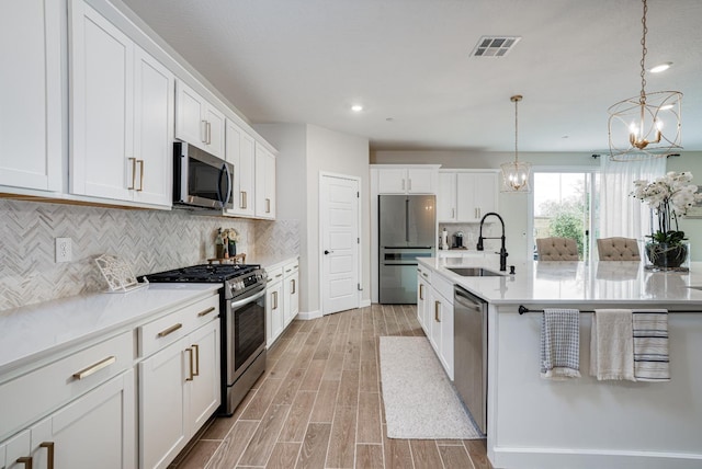 kitchen featuring visible vents, wood finish floors, appliances with stainless steel finishes, a notable chandelier, and a sink