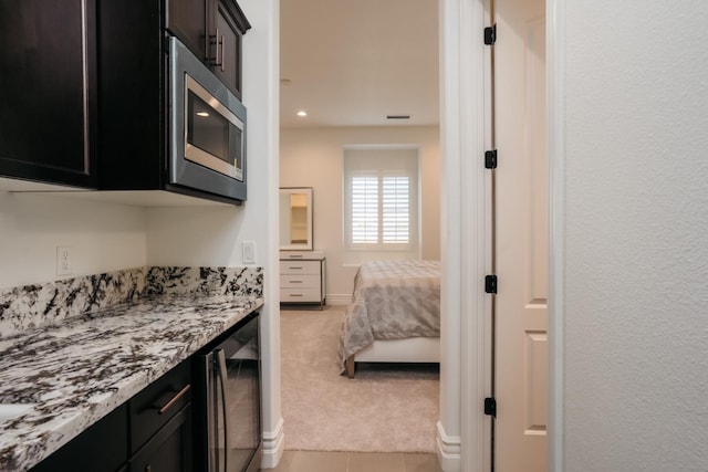 kitchen with stainless steel microwave, wine cooler, light colored carpet, and dark cabinetry