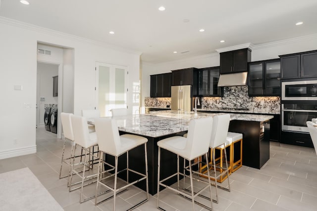 kitchen featuring visible vents, under cabinet range hood, stainless steel appliances, separate washer and dryer, and dark cabinets