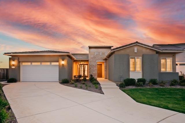 view of front facade with concrete driveway, stucco siding, a yard, a garage, and stone siding