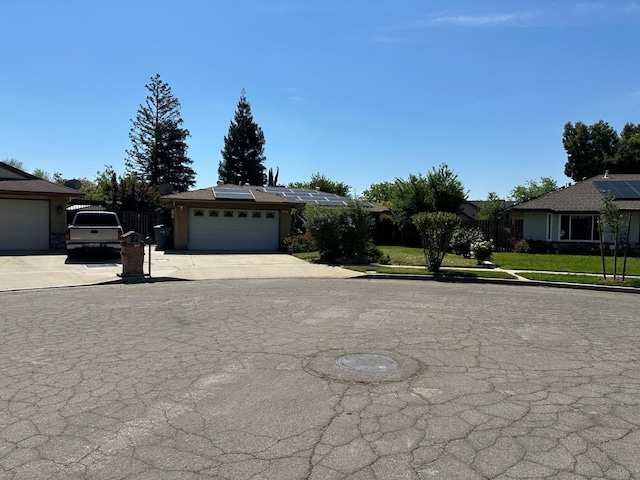 ranch-style house featuring roof mounted solar panels, driveway, an attached garage, and fence