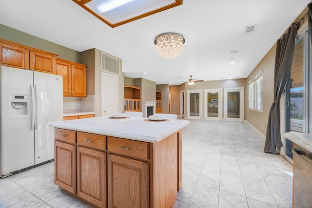 kitchen featuring visible vents, light countertops, ceiling fan with notable chandelier, white refrigerator with ice dispenser, and marble finish floor