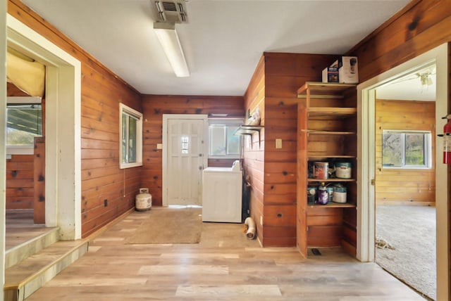 interior space with washer / clothes dryer, a healthy amount of sunlight, wood finished floors, and wood walls