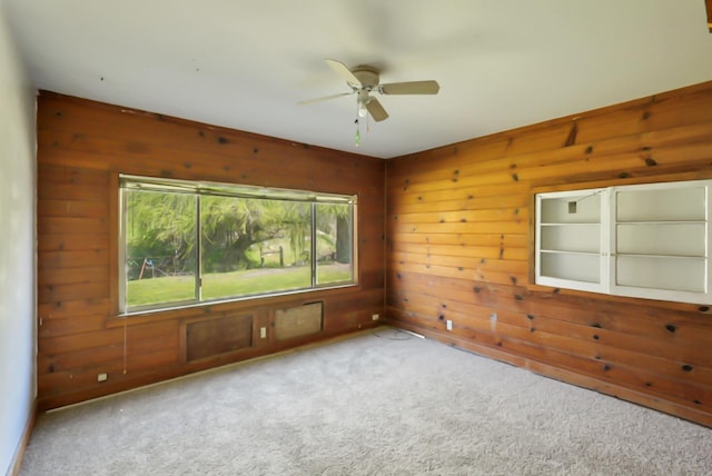 empty room with a healthy amount of sunlight, wood walls, ceiling fan, and carpet floors