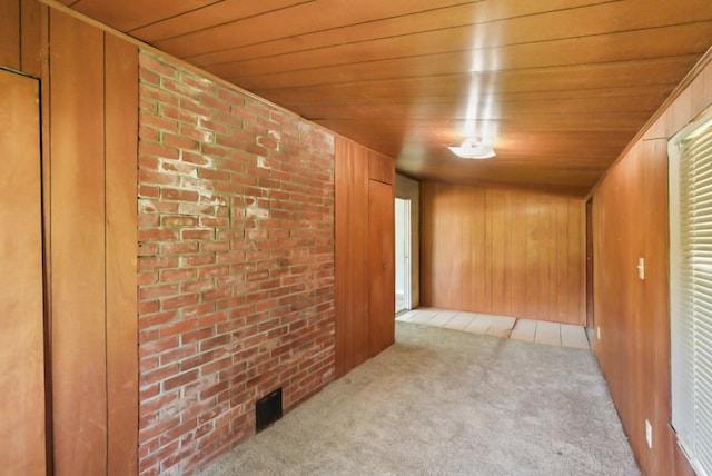 carpeted empty room with visible vents, wooden walls, wooden ceiling, and brick wall