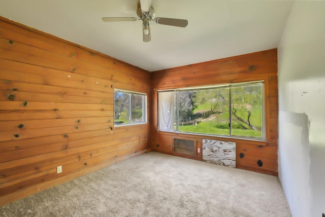 carpeted empty room featuring wood walls and ceiling fan