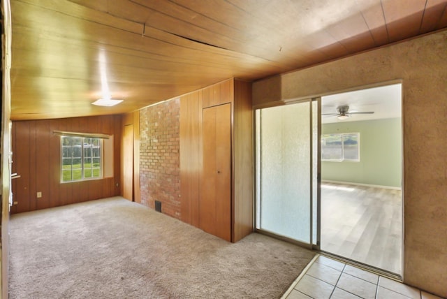 empty room with carpet, wood walls, a ceiling fan, and tile patterned flooring