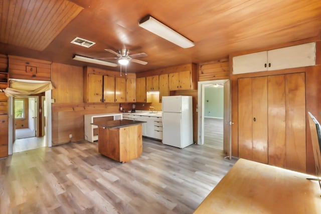 kitchen featuring visible vents, a kitchen island, freestanding refrigerator, wood ceiling, and wood walls