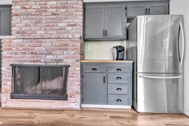 kitchen with light wood-style flooring, gray cabinets, a brick fireplace, and freestanding refrigerator