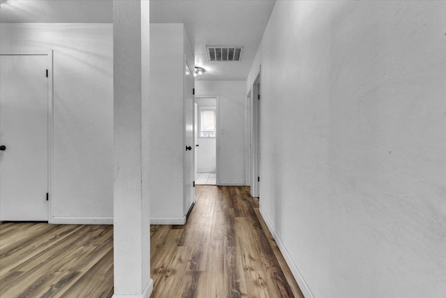 hallway with visible vents, baseboards, and wood finished floors