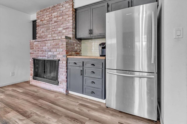 kitchen featuring gray cabinetry, a brick fireplace, light wood-type flooring, light countertops, and freestanding refrigerator