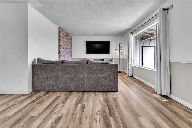 living area with visible vents, a textured ceiling, baseboards, and wood finished floors