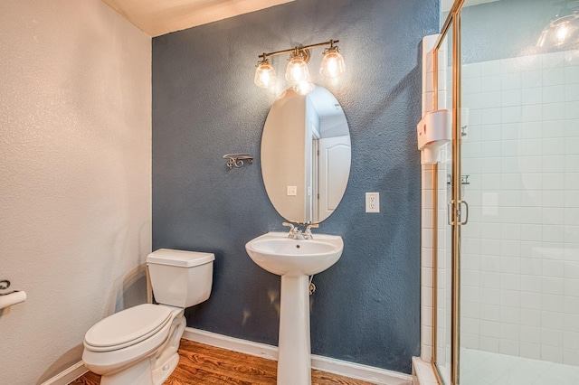 bathroom with toilet, wood finished floors, a stall shower, and a textured wall