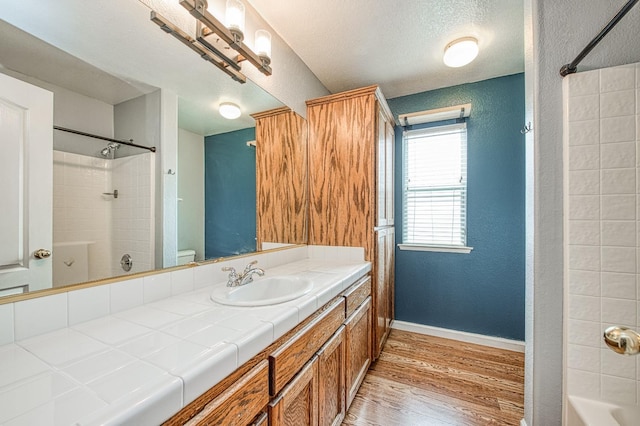 bathroom featuring a textured ceiling, wood finished floors, tub / shower combination, baseboards, and vanity