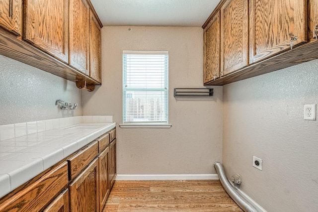 washroom with electric dryer hookup, light wood-type flooring, a sink, cabinet space, and baseboards