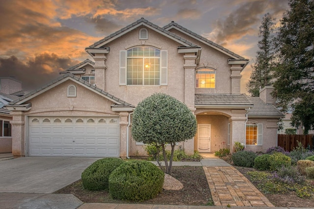 view of front of property featuring a tiled roof, concrete driveway, stucco siding, and fence