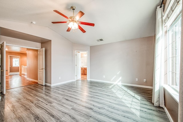 unfurnished bedroom featuring visible vents, connected bathroom, baseboards, vaulted ceiling, and wood finished floors