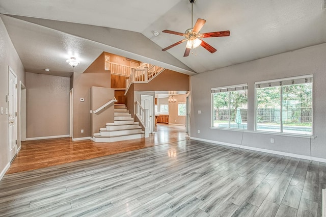 unfurnished living room featuring lofted ceiling, ceiling fan with notable chandelier, wood finished floors, baseboards, and stairs