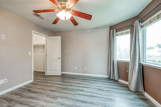 unfurnished bedroom featuring visible vents, a walk in closet, a ceiling fan, wood finished floors, and baseboards