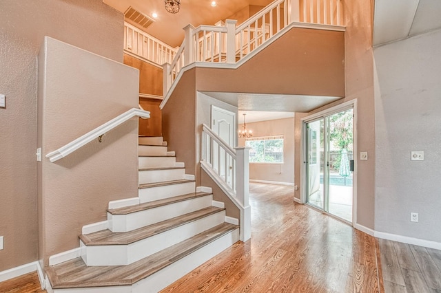 stairs with a chandelier, a high ceiling, baseboards, and wood finished floors