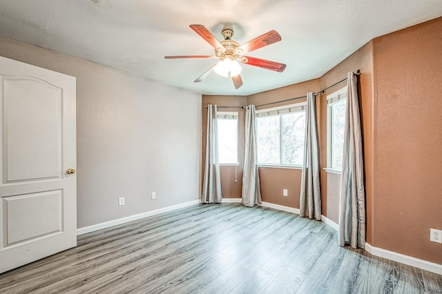 spare room with a ceiling fan, wood finished floors, baseboards, and a textured wall