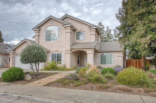 view of front of property with a tiled roof, an attached garage, fence, and stucco siding