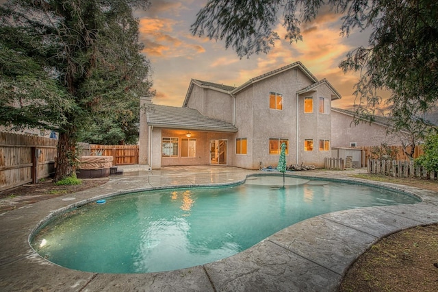 pool at dusk with a jacuzzi, a fenced in pool, a patio, and a fenced backyard